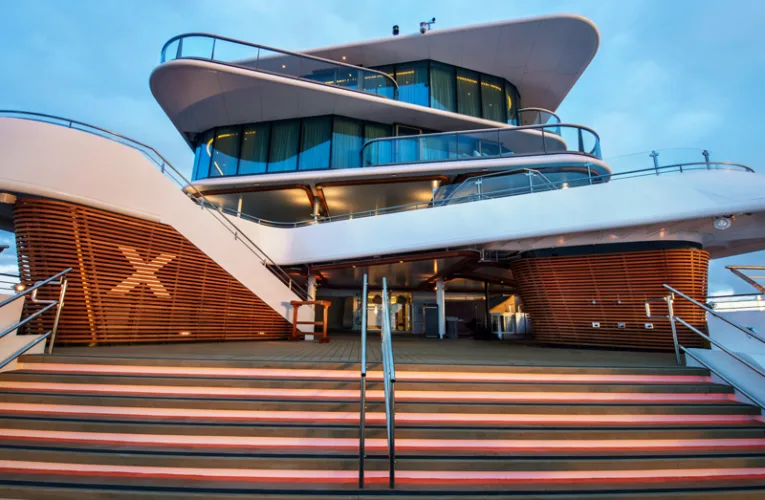 Cubierta exterior del megayate Celebrity Flora en Galápagos, mostrando sus escaleras iluminadas, diseño moderno con acabados en madera y niveles de suites de luj