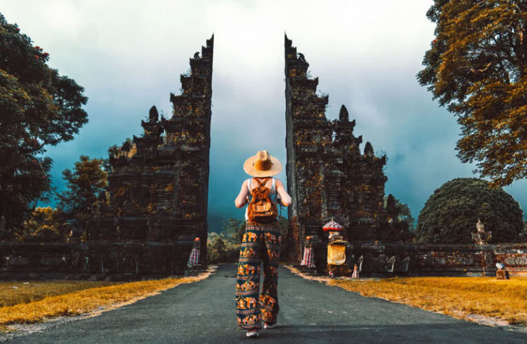 Una mujer caminando hacia unas puertas ornamentadas en un paisaje exuberante en Bali