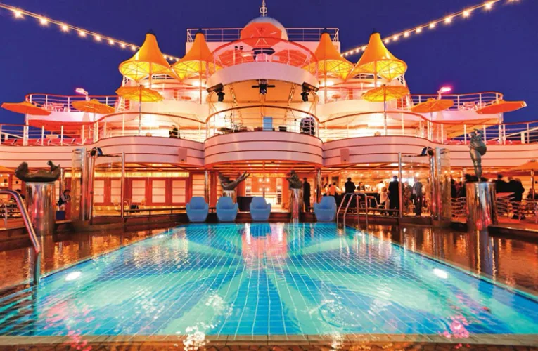 Bajo un cielo abierto, varias piscinas de gran tamaño se extienden sobre la cubierta, rodeadas de cómodas tumbonas y zonas para tomar el sol. El agua azul contrasta con el blanco brillante del barco, mientras jacuzzis burbujeantes invitan a relajarse con vista directa al mar.