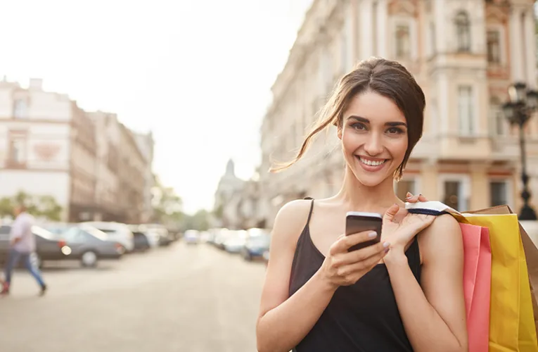 Mujer utilizando internet móvil en el extranjero con su smartphone frente a edificios clásicos.