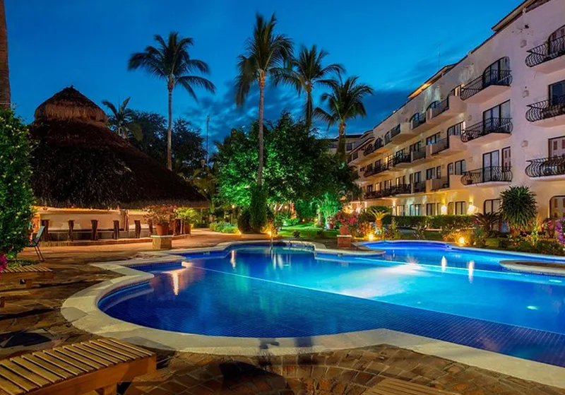 Vista nocturna de la alberca iluminada junto al paseo marítimo en Flamingo Vallarta Hotel.