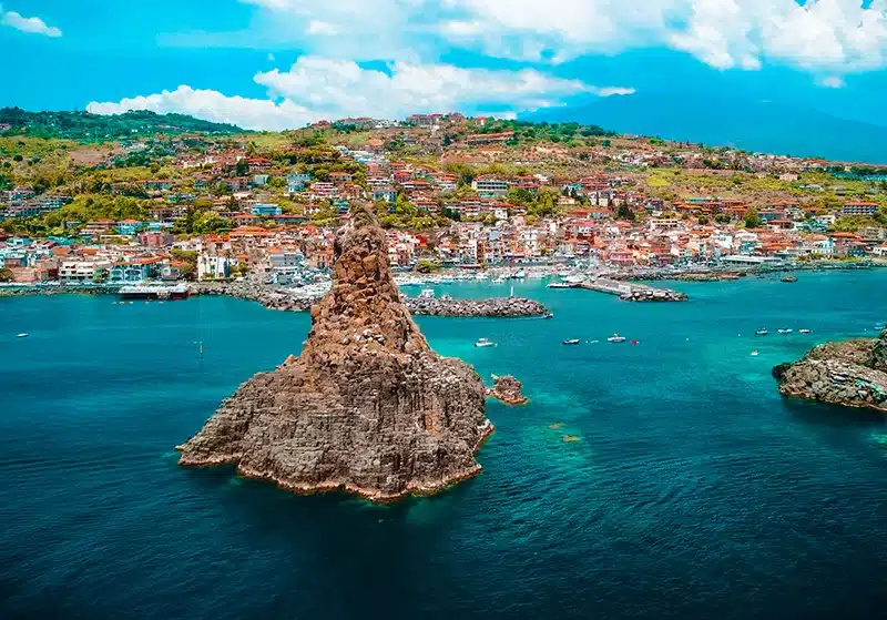 Serie de imponentes peñones y farallones escarpados de basalto negro volcánico que emergen verticalmente de las aguas azules y cristalinas del mar Jónico, situados muy cerca de la costa de la villa pesquera de Aci Trezza en Sicilia, Italia