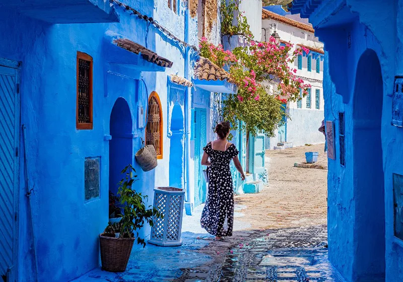 Una mujer camina por una pintoresca callejuela azul de Chefchaouen, Marruecos.