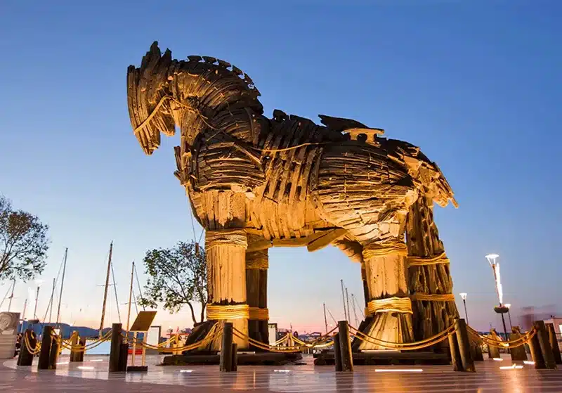 Gran escultura del Caballo de Troya (utilizada en la película de 2004) hecha de fibra de vidrio y acero con apariencia de tablones de madera oscura y desgastada, exhibida en la plaza pública del malecón peatonal de Çanakkale, Turquía, frente al mar